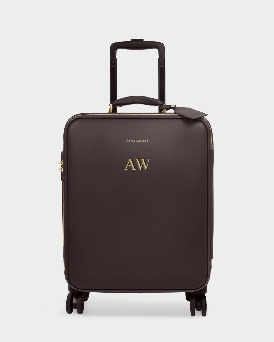 A dark brown softside spinner suitcase with an extended telescoping handle, gold-tone hardware, and a small gold logo on the front, shown against a light gray background.