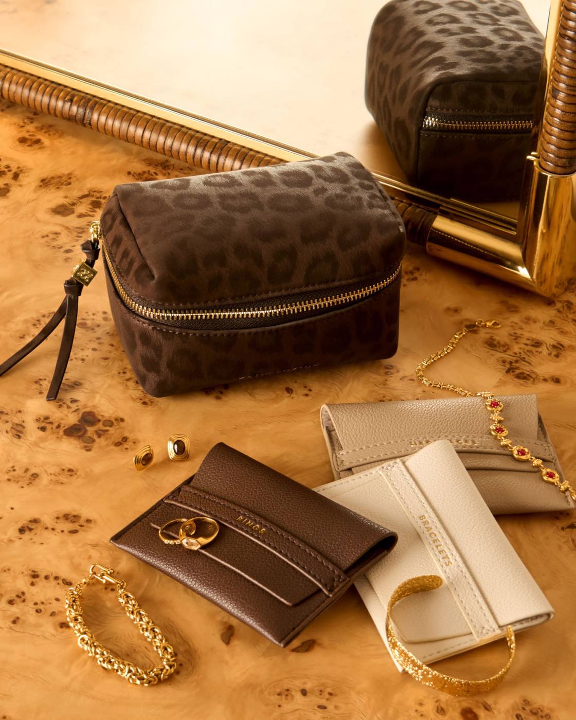 Leopard print makeup bag and various wallets on a wooden surface with gold jewellery.