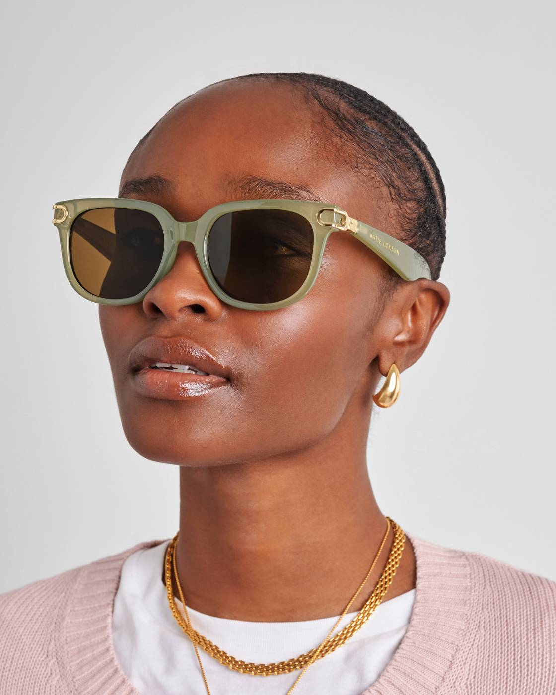 Woman wearing green sunglasses with gold frames on a plain background