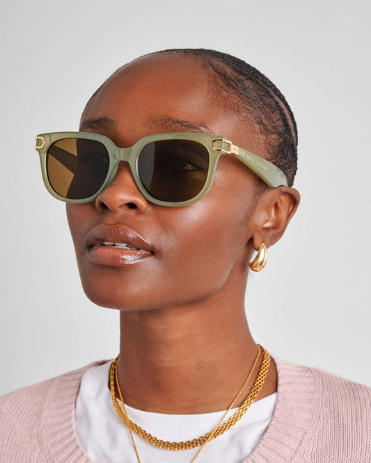 Woman wearing green sunglasses with gold frames on a plain background