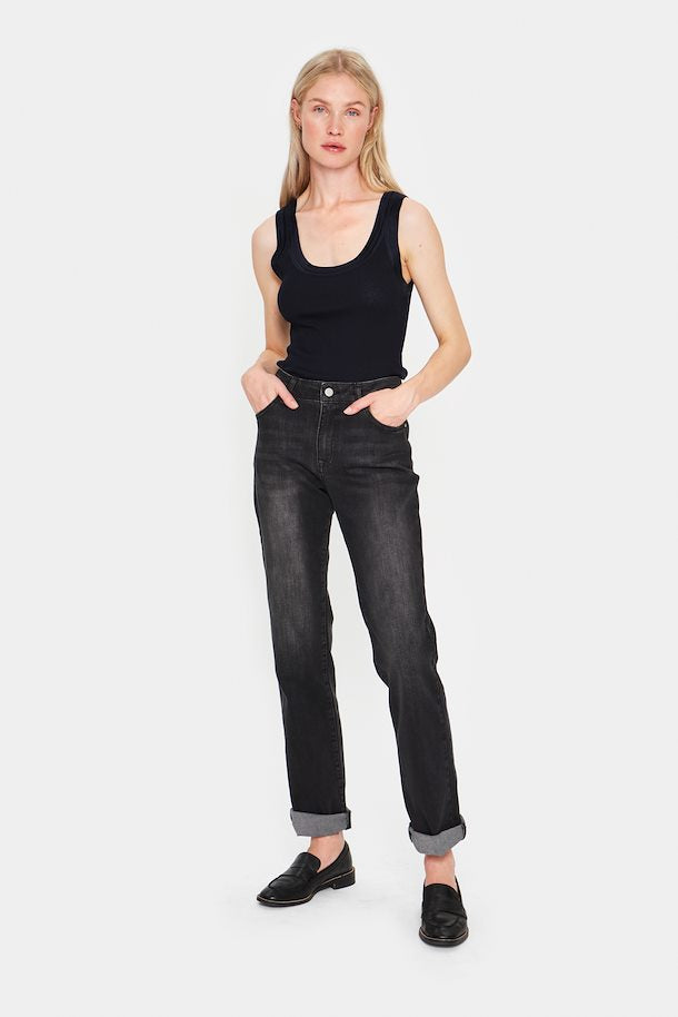 A woman standing wearing a dark blue tank top and blue jeans with a round neckline.