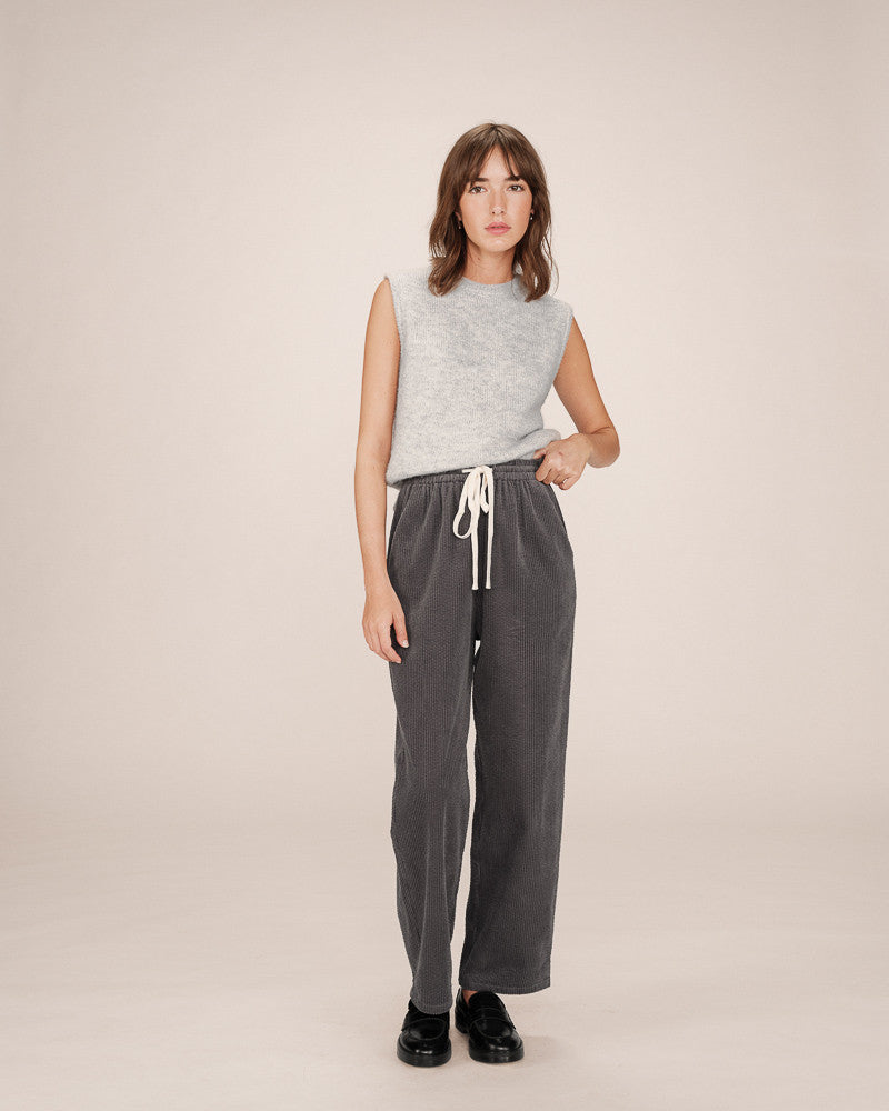 Woman wearing a sleeveless top and gray pants on a beige background