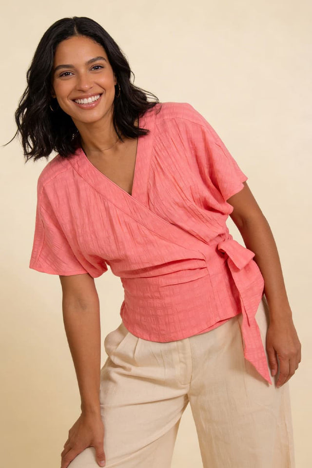 Woman wearing a pink top and beige pants against a beige background