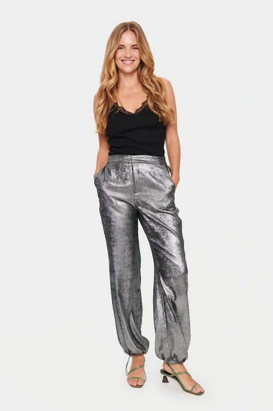 A person standing, wearing silver trousers and a black top.